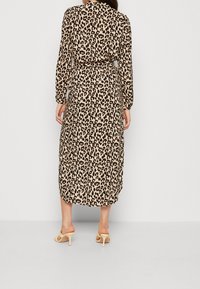 Robe mi-longue à imprimé léopard en beige et noir, avec manches longues et ceinture à la taille. Chaussures : sandales beige à lanières.