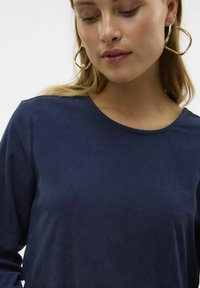 Mörkblå, ribbad långärmad topp med rund halsringning, som har en mjuk textur och lager med guldringörhängen med pärlor.