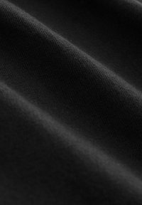 Close-up of soft, smooth black fabric with visible fine knit texture and gentle folds creating light and shadow contrasts.