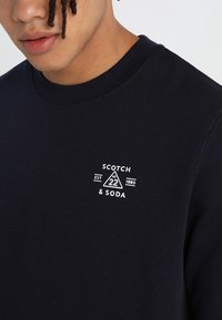 Sudadera navy de algodón, con un cuello redondo de canalé y un logotipo impreso en blanco con elementos geométricos en el pecho.
