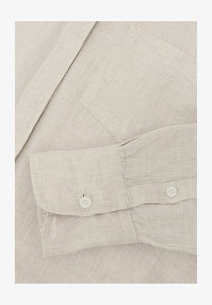 Light beige linen shirt sleeve with buttoned cuff and chest pocket, showing fabric texture and stitching details.