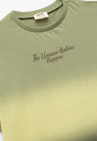 Camiseta de manga corta en degradado verde, con el texto "El Viajero de la Naturaleza Invisible" en marrón. Tejido suave y cuello redondo.