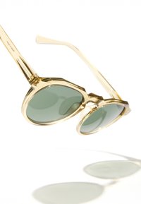Zlatne, prevelike sunčane naočale s zelenim staklima, s geometrijskim okvirom i glatkom teksturom. Naočale imaju elegantne, blago zakrivljene drške.