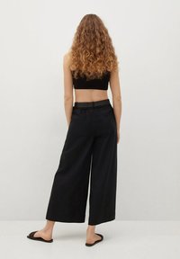 Černé kalhoty s širokými nohavicemi a elastickým pasem, s hladkou texturou a minimalistickým designem, z pohledu zezadu.