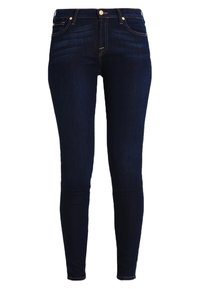Jeans skinny de denim azul escuro, com um design ajustado, detalhes de costura visíveis, fecho frontal com botão e cinco bolsos.