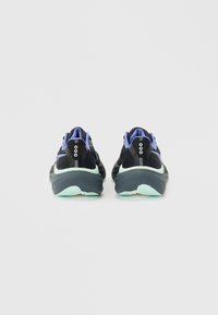 Ζευγάρι μαύρα και μωβ αθλητικά παπούτσια με παχιά σόλα σε μέντα-πράσινο, φωτογραφημένα από πίσω πάνω σε ένα απλό ανοιχτό γκρι φόντο.