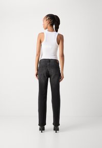 Jeans neri a gamba dritta con una texture sbiadita, cinque tasche e una toppa in pelle marrone sul retro. Abbinati a una canotta bianca.