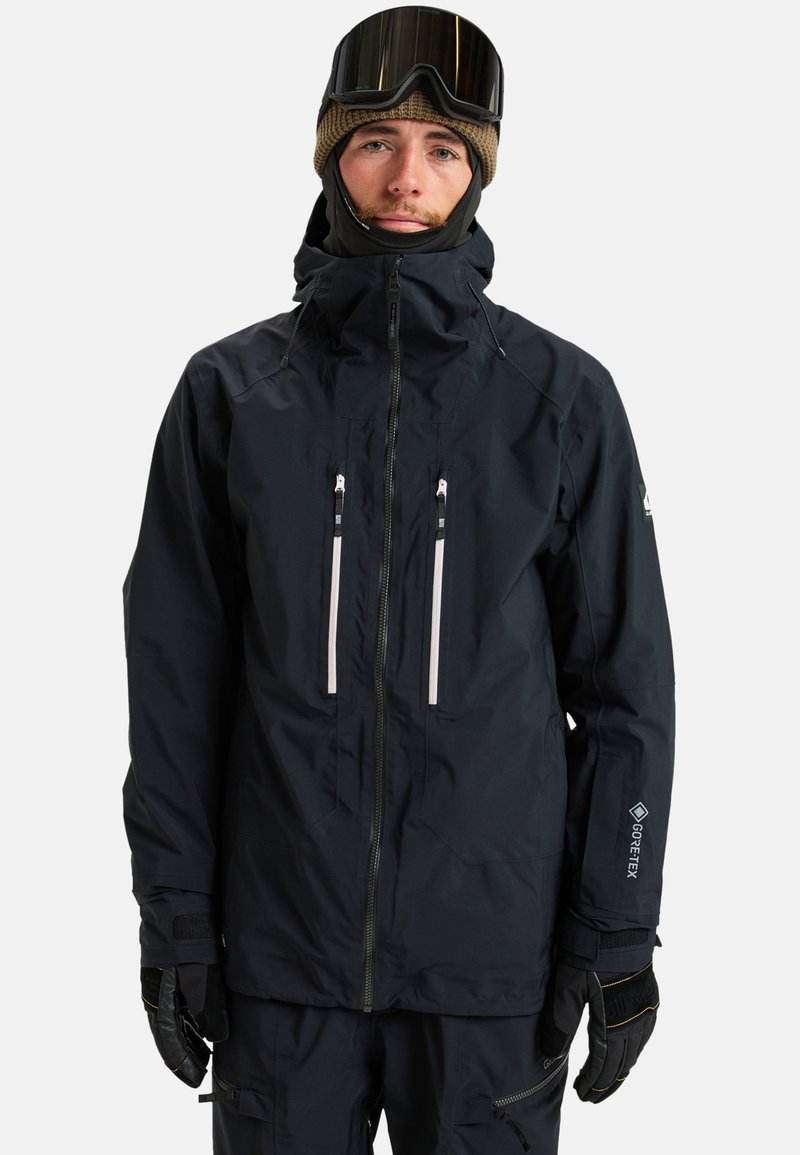 Schwarze wasserdichte Jacke mit hohem Kragen und verstellbarem Kapuzen, ausgestattet mit zwei mit Reißverschluss versehenen Brusttaschen und GORE-TEX-Branding am Ärmel.