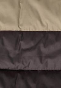 Tissu matelassé avec une surface texturée, présentant une section supérieure beige et une section inférieure marron foncé, disposées en bandes horizontales.