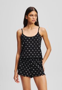 Conjunto de dos piezas negro que incluye una blusa sin mangas con un escote redondo y un bajo con volantes, acompañada de unos pantalones cortos a juego, ambos decorados con un pequeño patrón.