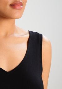 Haut noir sans manches avec un col en V, doté d'un tissu lisse et léger ainsi que de bords nets. Texture de peau visible au niveau de l'encolure.