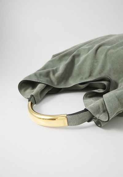 Grön mockaväska med ett böjt handtag i guldmetall. Texturen är mjuk och något skrynklig, med svart kant längs sömmarna.