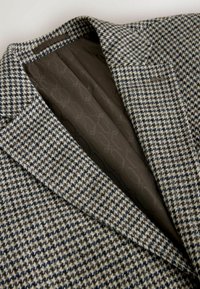 Houndstooth-mustriga bleiser pruuni, halli ja meriini tooni, millel on tumepruun vooder, millel on peen geomeetriline muster.