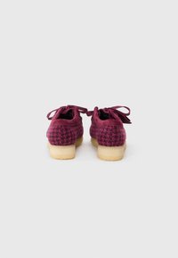 Pantofi texturați violet cu un model houndstooth, având vârf rotund și șireturi din material, așezați pe un toc rotund de culoare bej deschis.