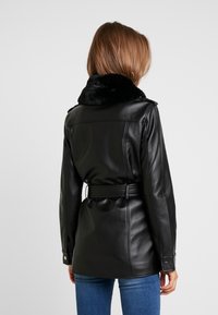 Chaqueta negra de cuero sintético con cuello de piel sintética, cintura con cinturón y puños abotonados; textura suave con un diseño ajustado y detalles de costuras en la parte trasera.