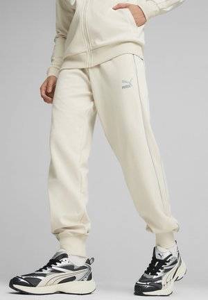 Person trägt off-white Puma Jogginghose und silber-schwarze Puma Sneaker, steht mit einer Hand in der Tasche.