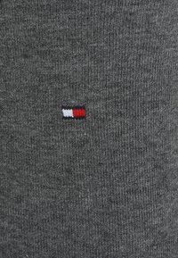 Grau geripptes Gewebe mit einem kleinen in Rot, Weiß und Blau gestickten Logo auf der linken Seite, das eine glatte Textur und enge Nähte zeigt.