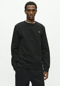 Black sweatshirt with a round neckline and ribbed cuffs, featuring a small logo on the left chest. Smooth texture and relaxed fit.