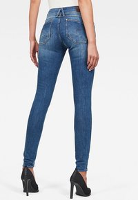 Tunna blå jeans med medelhög midja, som har bakfickor och en svart högklackad sko delvis synlig i nederkant.