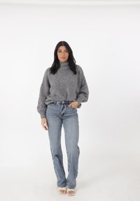 Grijze, gebreide trui met een hoge halslijn en ballonsleeves, gecombineerd met lichtblauwe, hoge taille jeans en witte sandalen.