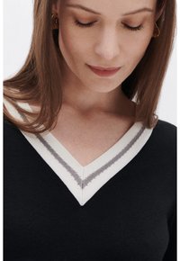 Maglione nero a collo a V con bordo a coste bianco e grigio a contrasto. La trama a maglia è morbida e la vestibilità è aderente al corpo.