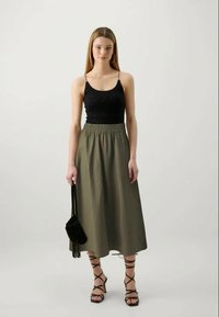 Top de renda preta, saia midi verde oliva com cintura elástica, bolsa de franjas preta e sandálias strappy pretas. Design limpo.