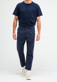 Navyblauw t-shirt met korte mouwen en een borstzak, gecombineerd met navy elastische broeken en crèmekleurige sneakers, met opgerolde mouwen.