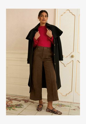 Sort dobbeltbrystet frakke, rød ribbet top, brune højtsiddende brede bukser, leopardmønstrede flade sko, gyldne runde øreringe. Tekstureret og skræddersyet design.