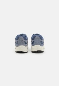 Basket en mesh bleu et en daim avec une semelle en caoutchouc crème, présentant des découpes pour l'aération et un talon texturé. Logo Nike à l'arrière.