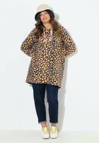 Haut à manches longues en navy avec un imprimé léopard jaune et orange, doté d'un cordon de serrage, associé à un denim retroussé et des baskets blanches.