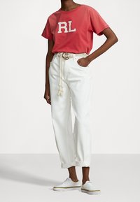 Röd t-shirt med "RL"-logotyp, vita högmidjade byxor med uppvikta fållar och vita sneakers med gula detaljer. Repbälte ger struktur.