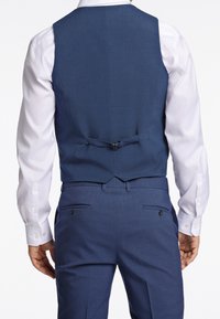 Mörkblå skräddarsydd väst med en slät yta, utrustad med ett baksidespänne, bärs över en vit skjorta. Elegant och välsittande design.