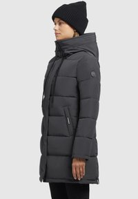 Donkergrijze gewatteerde jas met een hoge kraag, verticale zigzagstiksels, ritszakken aan de zijkant en een logopatch op de linkermouw.