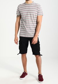 Šedé pruhované tričko s červenými a modrými pruhy, spárované s černými cargo šortkami s bočními kapsami a burgundskými teniskami.