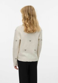 Pulover iz pletenine v kremni barvi z majhnimi sivi srčkastimi vzorci, okrogli izrez, ter rebrasti manšeti in spodnji del. Ujemajo se z črnimi hlačami.