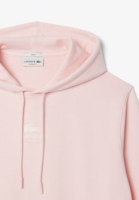 Sudadera con capucha de Lacoste en rosa claro con un corte clásico, que presenta un logo en la parte frontal, cordones y una textura suave.