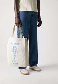 Cotton tote bag in light cream with blue graphic of an ice cream cone and text "ICE CREAM PLEASE." Reinforced handles, rectangular shape.