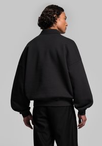 Sweatshirt noir oversize avec des coutures d'épaule tombantes et des poignets côtelés, présentant une texture lisse et un design minimaliste.