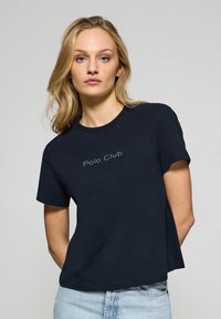 T-shirt noir à manches courtes en coton, avec une coupe décontractée et le texte "Polo Club" dans une couleur subtile et contrastante sur le devant.