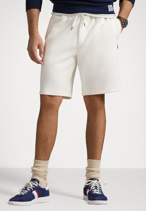 White cotton shorts with an elastic waistband and drawstring. Model wears navy sneakers with white soles and beige crew socks.