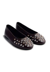 Zapatos planos de cuero marrón con puntera redonda, adornados con tachuelas metálicas de diferentes tamaños en tonos plateado y oro rosa a lo largo de la parte superior.
