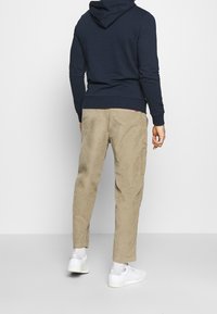 Felpa blu con cappuccio, abbinata a pantaloni in corduroy beige con tasca laterale. Sneakers bianche completano l'outfit.