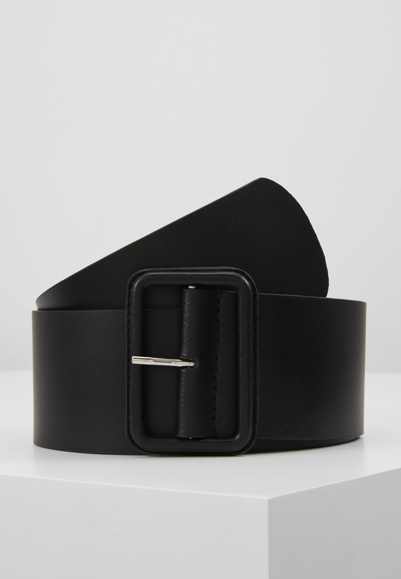 Ceinture large en cuir noir avec une boucle rectangulaire assortie et une épingle en métal argenté, présentée enroulée sur une surface blanche sur un fond uni.