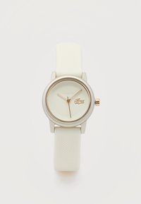 Λευκό ρολόι χειρός Lacoste με στρογγυλό καντράν, χρυσά δείκτες και υφασμένος ιμάντας από σιλικόνη σε ανοιχτό φόντο.