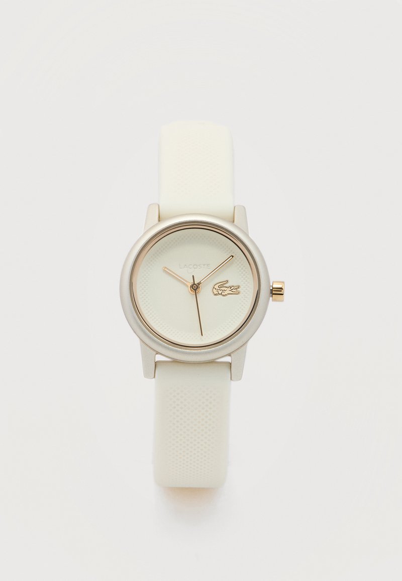 Λευκό ρολόι χειρός Lacoste με στρογγυλό καντράν, χρυσά δείκτες και υφασμένος ιμάντας από σιλικόνη σε ανοιχτό φόντο.