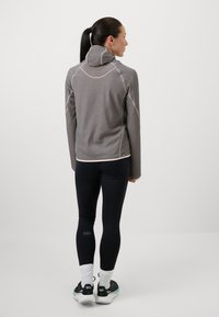 Kerge hall fliisist pullover kõrge kaelusega, kontrastsete õmblustega ja mugava lõikega, koos mustade retuuside ja tossudega.