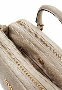 Sac en cuir beige clair avec deux compartiments zippés, des accents en métal doré et une finition texturée. Comprend une poignée supérieure robuste.