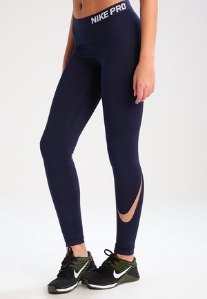 Les leggings Nike Pro navy présentent une taille haute, un design épuré et une accentuation par une découpure sur le côté. Assortis à des chaussures de sport noires.