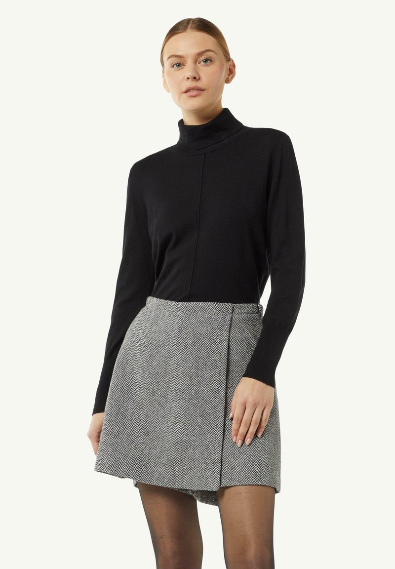 Black turtleneck sweater paired with a gray houndstooth wrap skirt. The outfit features long sleeves and a fitted silhouette.
