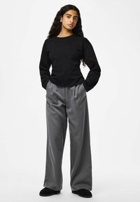 Chemise noire à manches longues, pantalon large rayé gris, tissu doux, coupe décontractée. Accessoires : chaussons noirs. Look simple et décontracté.